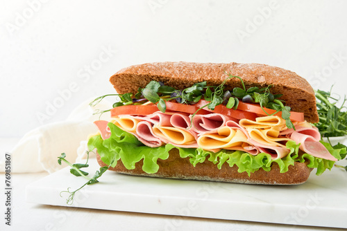 Sandwich. One fresh big submarine sandwich with ham, cheese, lettuce, tomatoes and microgreens on light background. Healthy breakfast theme concept, school lunch, breakfast or snack.