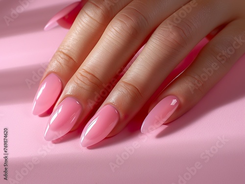 A person's hand with well-groomed nails with semi-permanent pink nail polish under natural daylight. A woman's hand with pink painted nails.