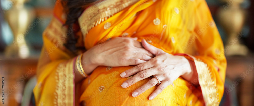 A close-up of a glowing Indian woman her hands tenderly caressing her belly