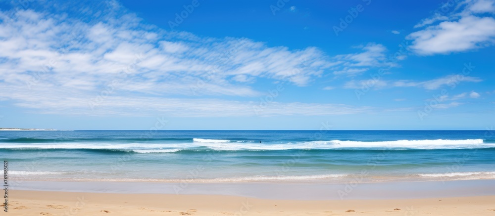 A hazy image of a beach with gentle waves rolling in under a sunny sky, creating a tranquil scene of coastal and oceanic landforms on a natural landscape