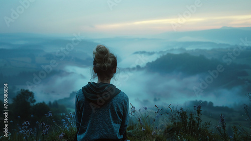 A woman overlooking a misty valley the image focused on her silhouette against a palette of soft lavenders and cool blues