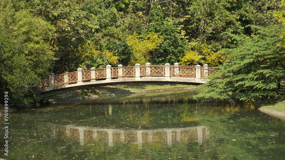A reflection on the water surface of a bridge over a river in a park.