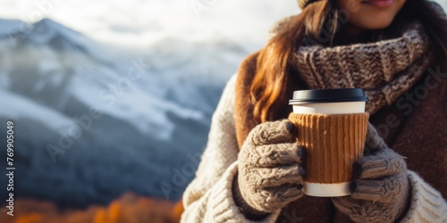 A girl holds a mug of hot drink, coffee, tea against the background of winter mountains in the camp. Generative AI. © Mountains Hunter