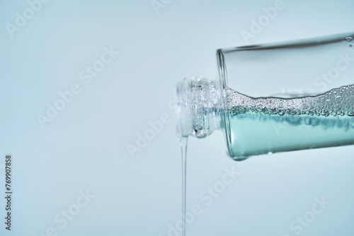 Cosmetic bottle from which serum is pouring on a blue background.