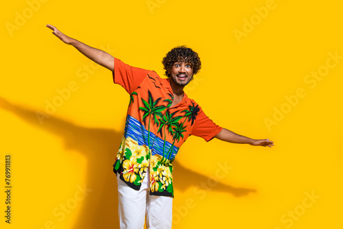 Photo of astonished funky man with afro hairdo dressed print shirt holding palms like wings isolated on vivid yellow color background