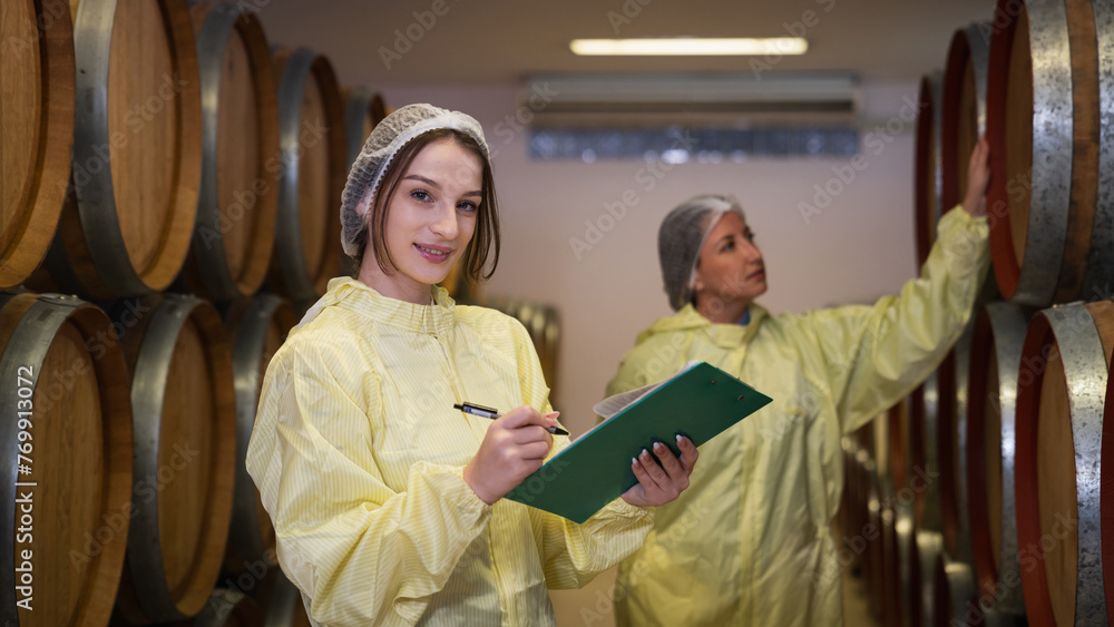 Portrait of Workers examining barrels in a winery. Woman tasting and smelling wine in a cellar with wooden barrels.