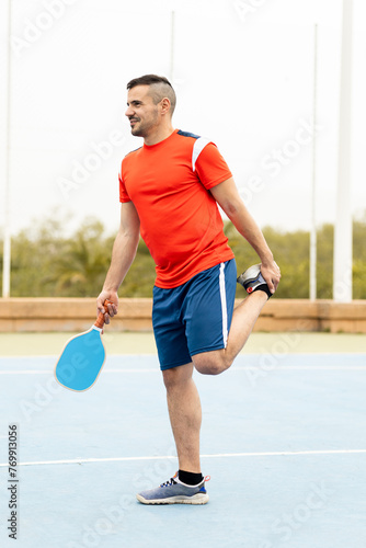 An adult man between 30 and 40 years old is playing a game of pickleball outdoors.The young man dressed in sportswear is stretching one leg after training.Pickleball concept. ©  Yistocking