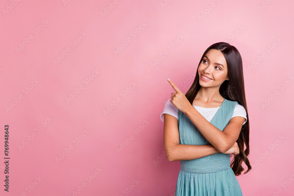 Happy young smiling woman wearing looking at camera pointing finger away at copy space showing aside presenting advertising offer standing isolated at pink background Happy young smiling woman wearing looking at camera pointing finger away at copy space showing aside presenting advertising offer standing isolated at pink background