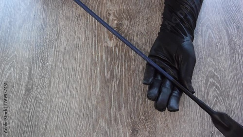 Horizontal Full HD video. Top view. Woman holds riding hunting crop, stack, short thin cane with leather loop at end, whip for horse riding, adult love games. Female hand in black gloves close up. Toy