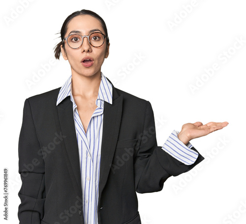 Confident young Caucasian businesswoman on studio background impressed holding copy space on palm. photo