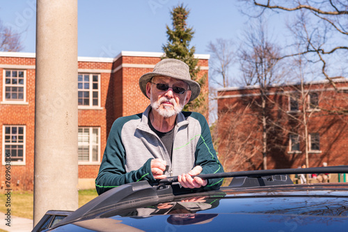 roof rack cross bars: senior citizen man beard hat sunglasses sets the folding cross bars of a built in roofrack in place on a blue station wagon room for text photo