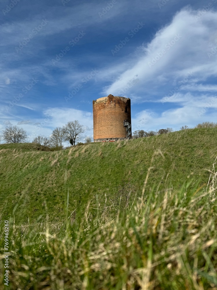 ancient red brick tower on a hill against the background of the sky with clouds