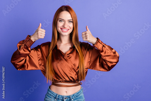 Portrait of nice young woman show thumb up empty space wear brown shirt isolated on purple color background © deagreez