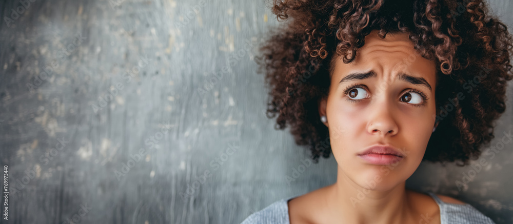 Fototapeta premium A close-up of a young woman with curly hair looking upwards with a worried and thoughtful expression.