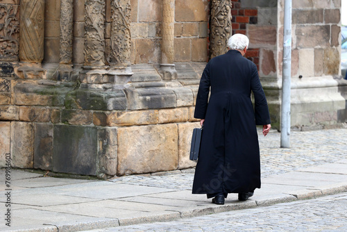 Ksiądz katolicki z teczką idzie ulicą. 