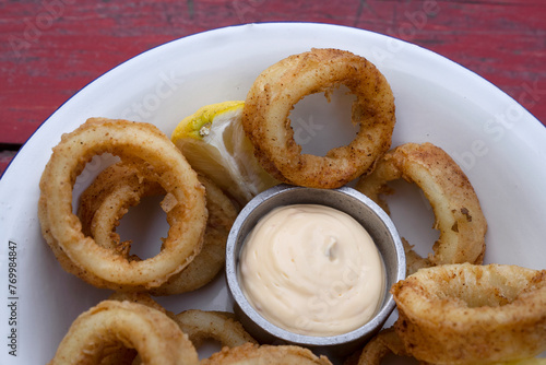 Deep fried seafood. Top view of delicious fried squid rings with lemon and a dipping sauce in a white bowl.	