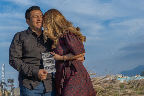 Expecting Parents with Ultrasound Photo Embracing Outdoors, latin young couple