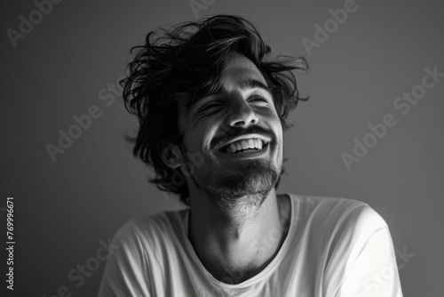 Black and white portrait of a joyful young man with messy hair, laughing and looking to the side, against a plain background. photo