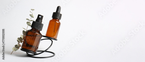 Bottles of cosmetic products and eucalyptus branch on light background