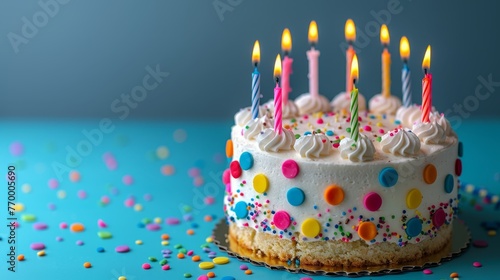   A colorful birthday cake with white frosting on a blue table, adorned with sprinkles and confetti