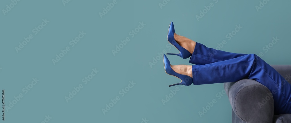 Legs of young woman in elegant high heels on sofa against blue background with space for text - obrazy, fototapety, plakaty 