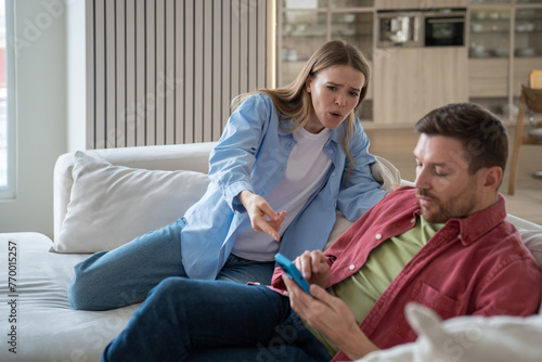 Fotografie Irritated nervous jealous woman shouts at husband accusing of cheating and betrayal pointing finger at cellphone