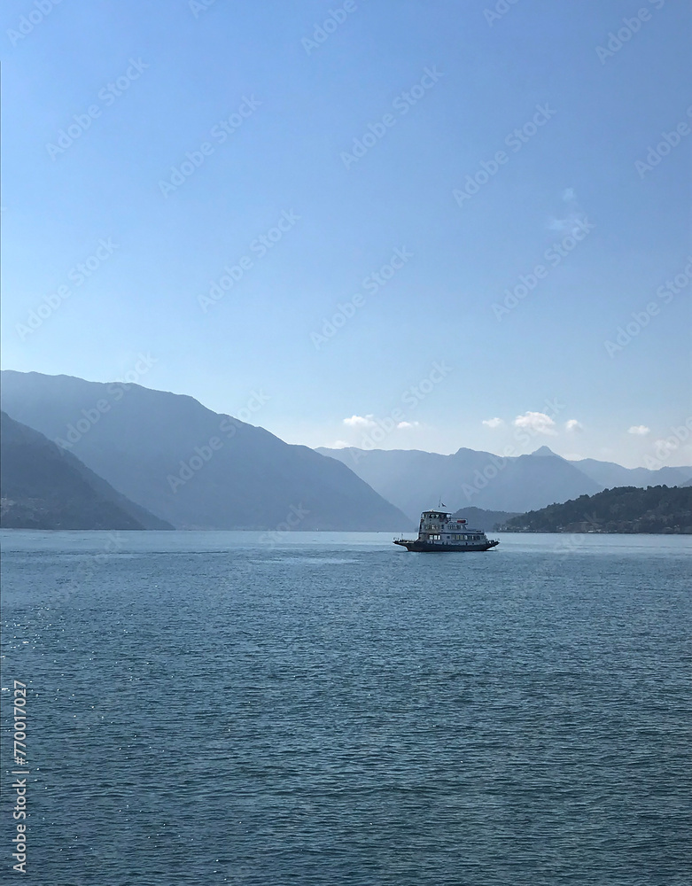 A ship sailing on the Lake of Como in the mountains on a summer day, blue sky and blue water with a ship
