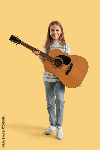 Teenage girl with acoustic guitar on yellow background