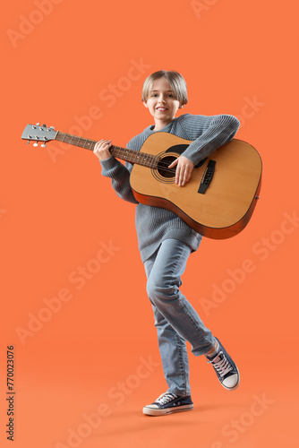 Little boy playing guitar on orange background