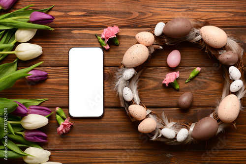 Composition with modern mobile phone, beautiful flowers and Easter wreath on wooden background