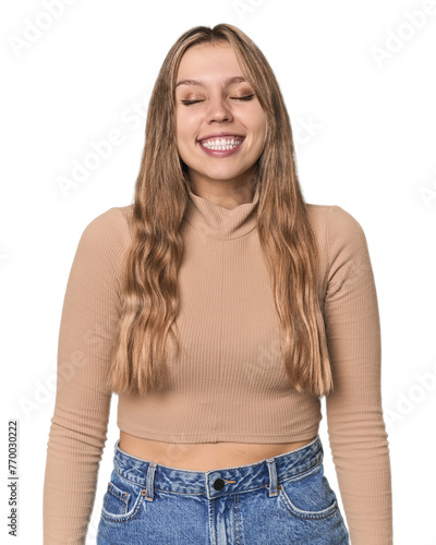 Studio portrait of a blonde Caucasian woman laughs and closes eyes, feels relaxed and happy. © Asier