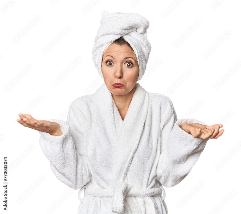 Caucasian woman in bathrobe and towel doubting and shrugging shoulders in questioning gesture.
