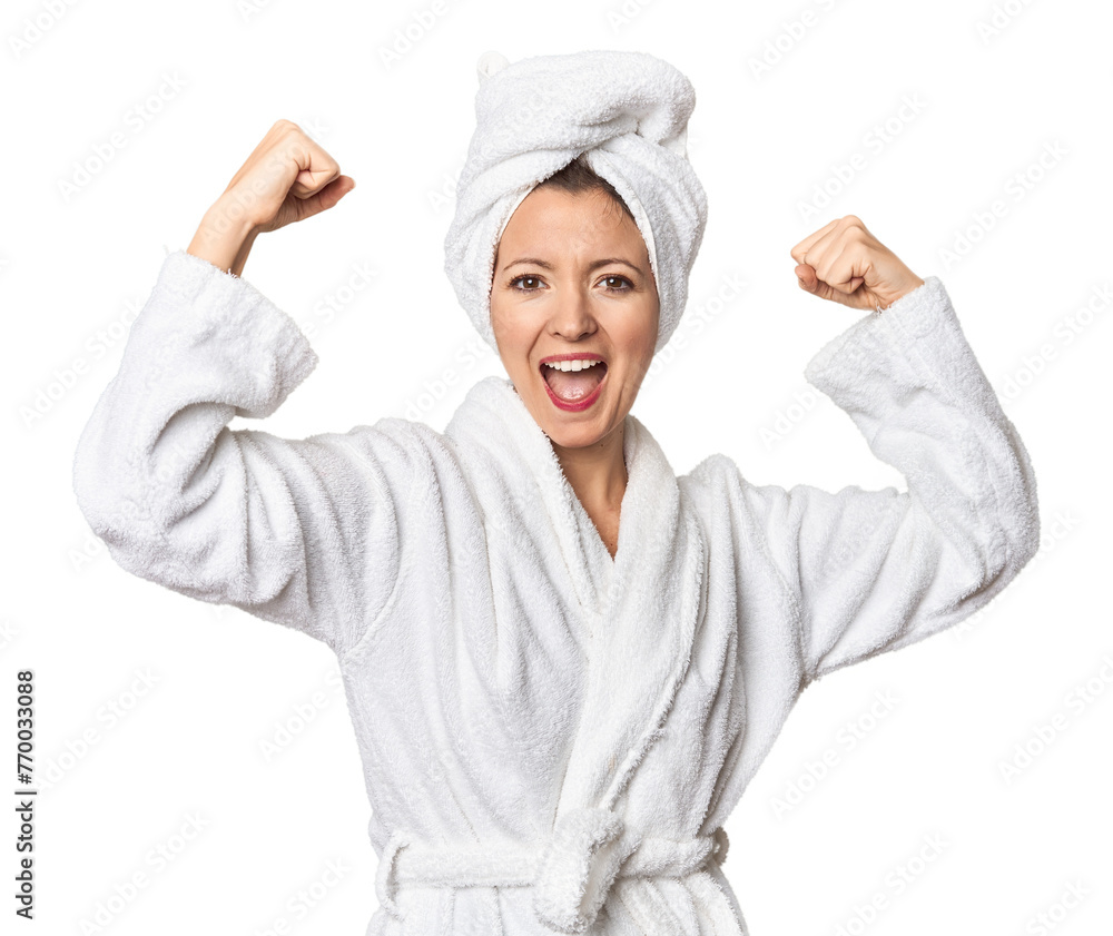 Caucasian woman in bathrobe and towel showing strength gesture with arms, symbol of feminine power Caucasian woman in bathrobe and towel showing strength gesture with arms, symbol of feminine power