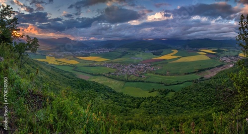 View from the hill of a spring landscape with fields of canola, grain and forests. Small villages in the valley, hilly landscape with dramatic sunset sky © Ivan