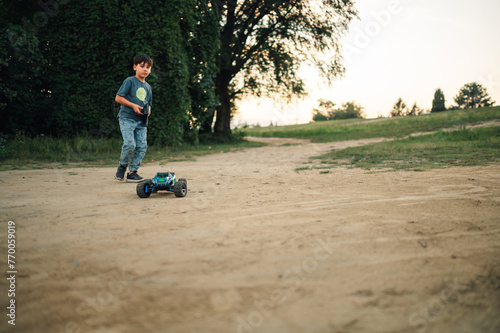 Boy running after a remote toy car he controls with a remoter outdoors photo