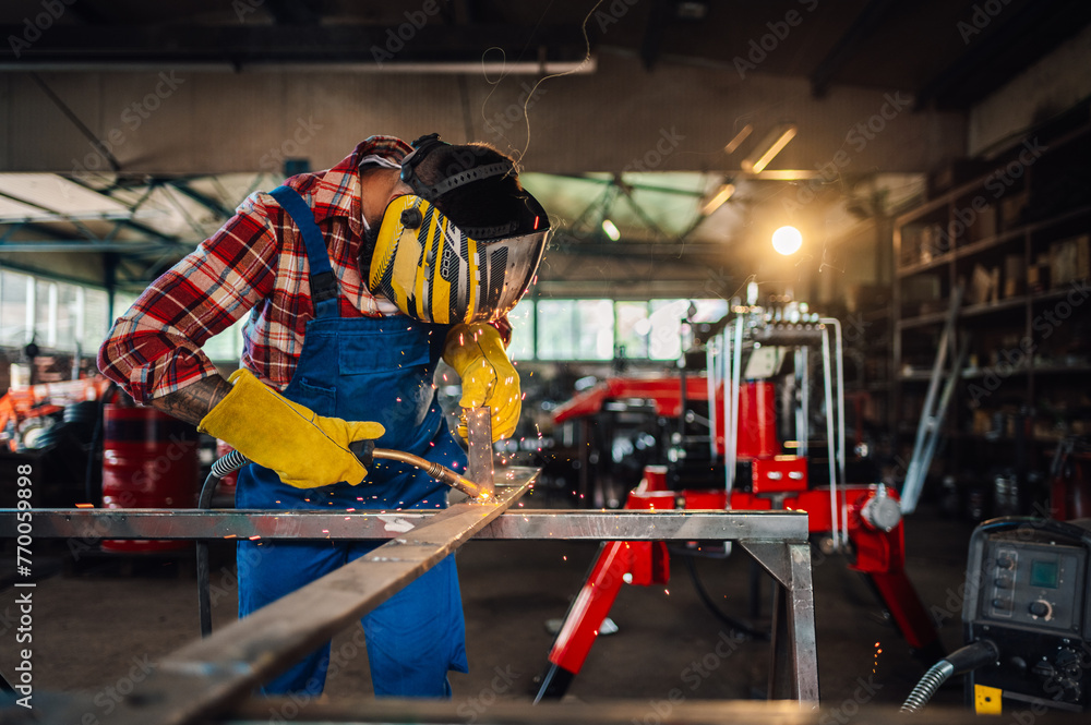 Worker wearing safety equipment while working on his welding machine. - obrazy, fototapety, plakaty 