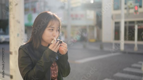 A young Japanese woman from Okinawa Prefecture in her 20s eating Okinawa street food pork egg rice balls on Kokusai Street in Naha City, Okinawa Prefecture 沖縄県那覇市の国際通りで沖縄のストリートフードのポークたまごおにぎりを食べる20代の沖縄 photo