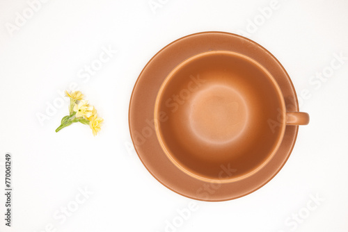 Xícara de café preto com espuma dourada, pires e xicara em terracota, bege, marrom, terra,  , pequeno ramalhete de pequenas flores amarelas fundo branco photo