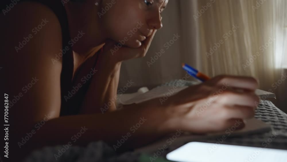 At night, the young woman lies on the bed and works, copying a notebook. At night, the young woman lies on the bed and works, copying a notebook.