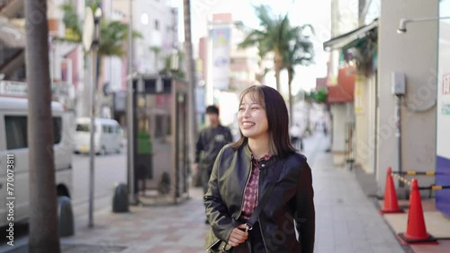 A young Japanese woman from Okinawa Prefecture in her 20s in winter clothes walking with a smile on Kokusai Street in Naha City, Okinawa Prefecture 沖縄県那覇市の国際通りで笑顔で歩く冬服の20代の沖縄県出身の若い日本人女性
 photo