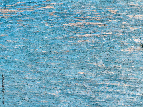 Close-up of a weathered blue painted wooden surface. The paint is peeling and cracking, revealing the natural wood grain underneath. The texture is rough and uneven.