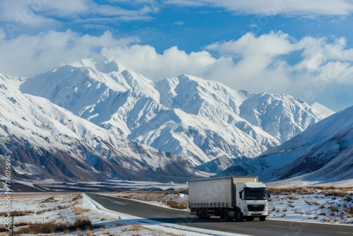 White truck cargo lorry on highway road in mountain landscape with snowcapped peaks and blue sky photo
