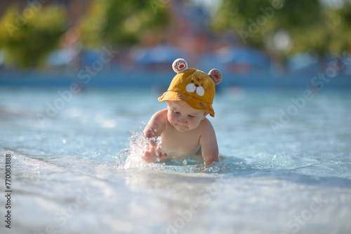 a little half a year old, a baby baby crawling on the water, smiling, outdoors, in a panama hat, in diapers, in the sun at the resort. © justoomm