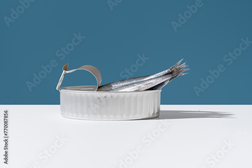 Fresh anchovies extend from an open can, set against a crisp blue background, illustrating a blend of natural and industrial themes