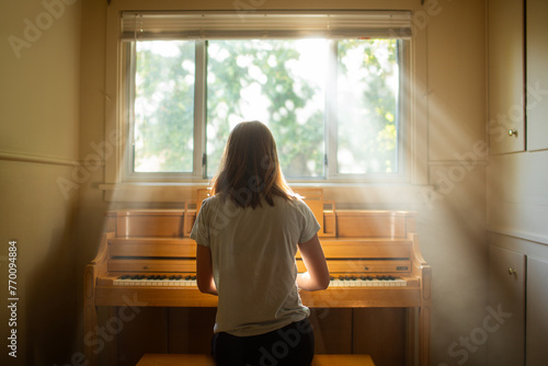 Young girl playing an old piano in front of a window
