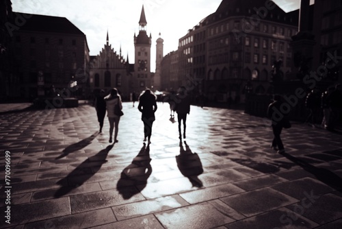 Silhouetted people walking in a city square with long shadows, dramatic lighting, and historic architecture in the background.