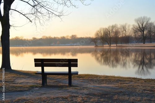 A single empty bench faces a serene lake, offering a quiet place for contemplation amidst the soft hues of a new day breaking