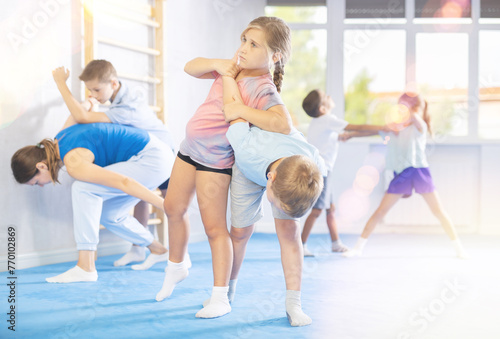 Preteen children practicing in pair self-defence movements with female trainer supervision