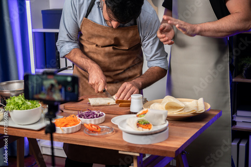 Cropped view of chef influencers presenting fresh salad roll on cooking step by step, streaming via smartphone on social media live channel, showing ingredients vegetable soft tortilla wrap. Sellable. photo