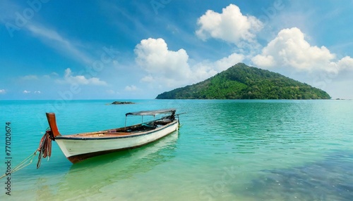 Boat in turquoise ocean water against blue sky with white clouds and tropical island. Natural landscape for summer vacation, panoramic view. 